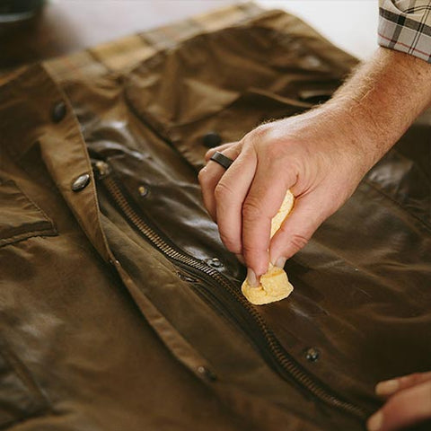 A hand wiping wax on to a Barbour Wax Jacket